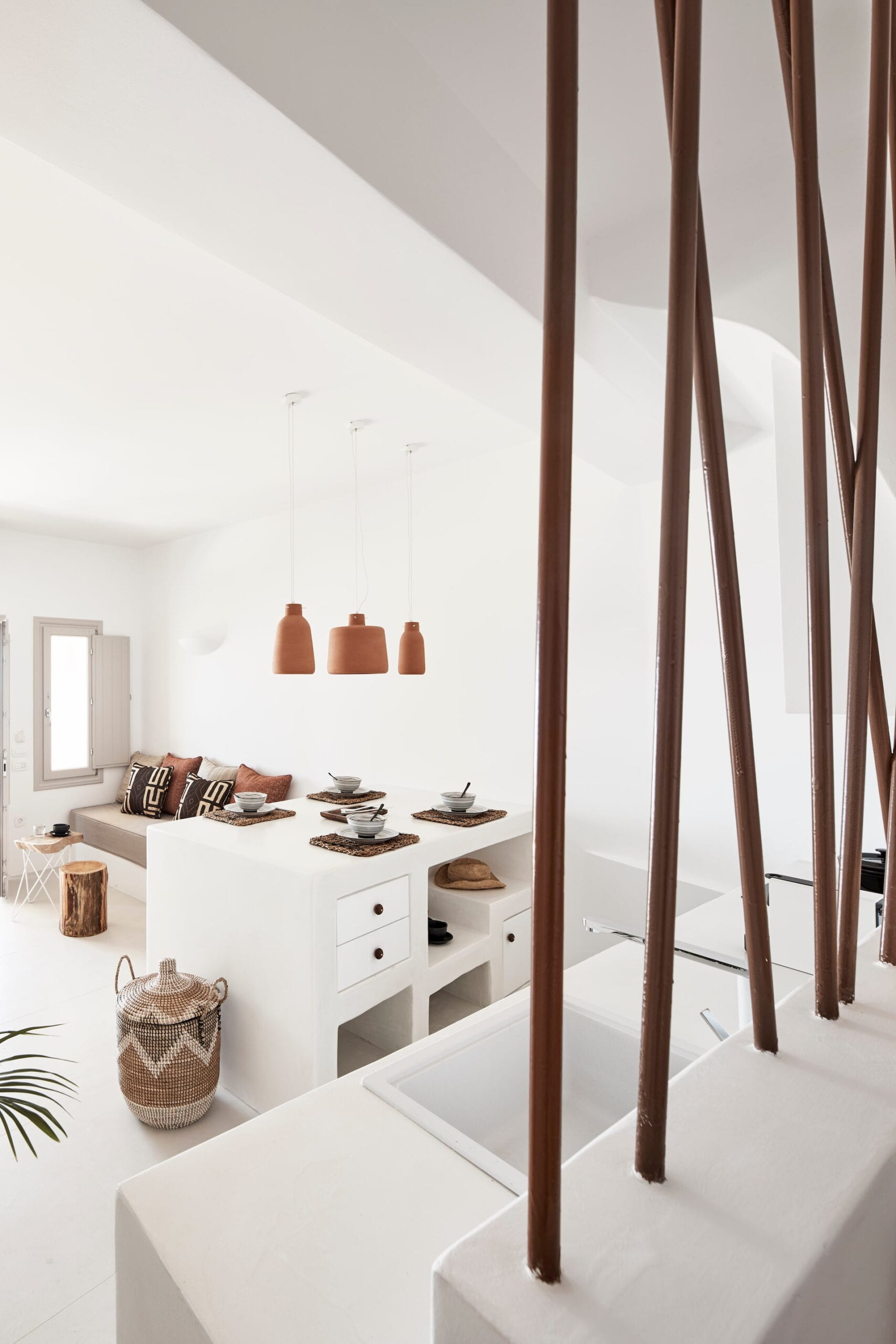 Whitewashed Cycladic living and dining space with terracotta pendant lamps and a floating staircase