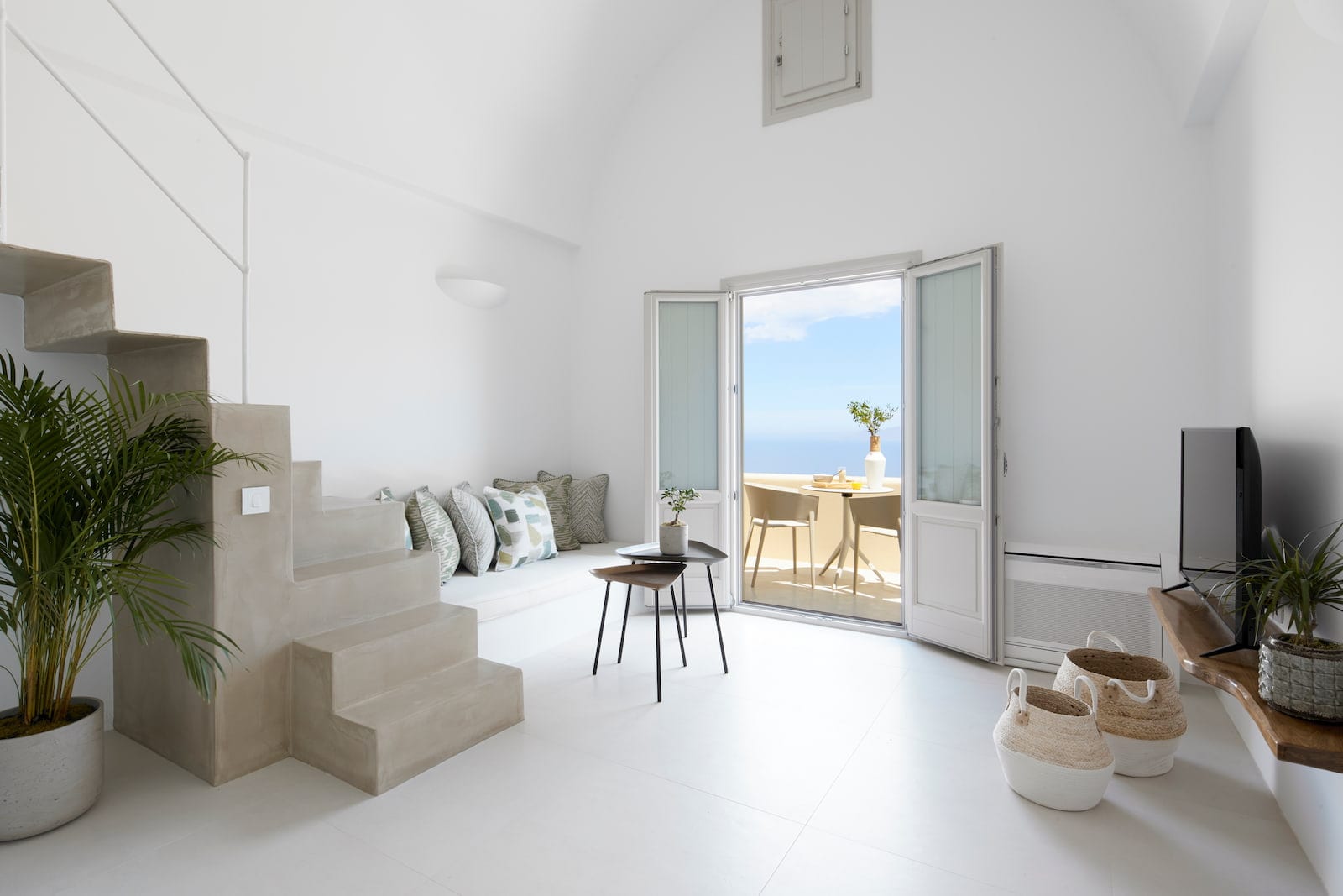 Whitewashed living space with a built-in cushioned bench and French doors opening to a sea-view terrace