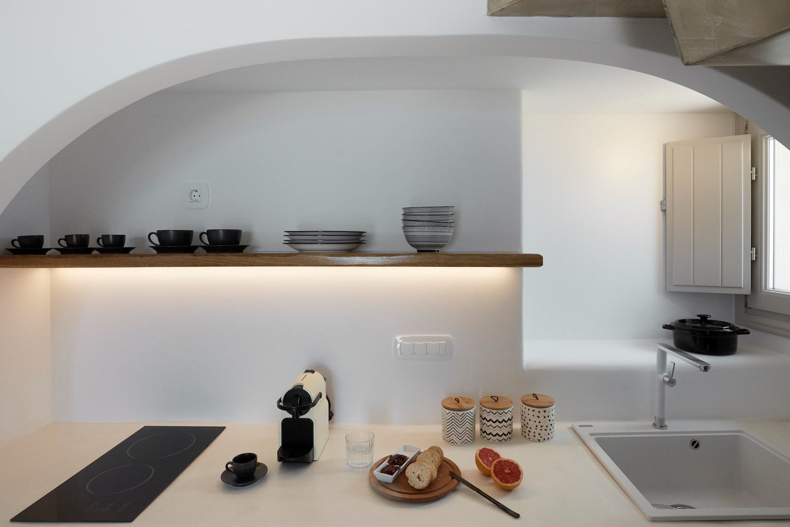 Compact kitchen niche with an oak shelf, black tableware, induction hob and a fresh Greek breakfast