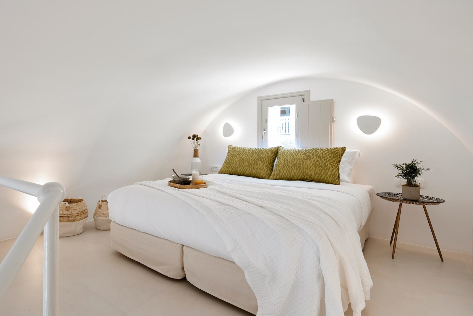 Arched loft bedroom with a plush white bed, olive-green cushions and a morning breakfast tray
