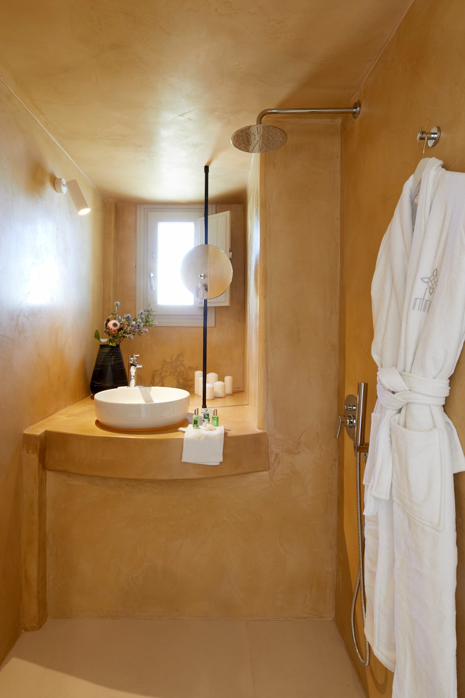 Ochre tadelakt bathroom with a round vessel sink, rainfall shower and monogrammed Infinity bathrobe