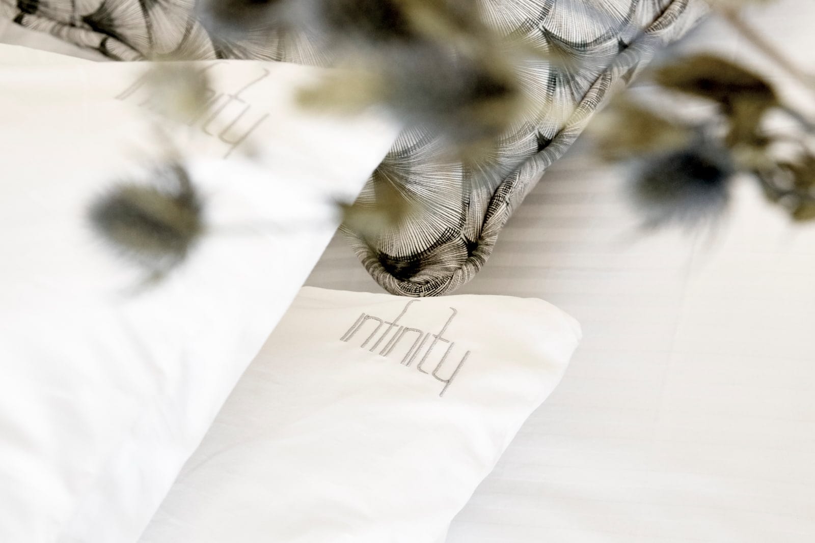 Crisp white pillows embroidered with the Infinity name, styled with feathery dried stems