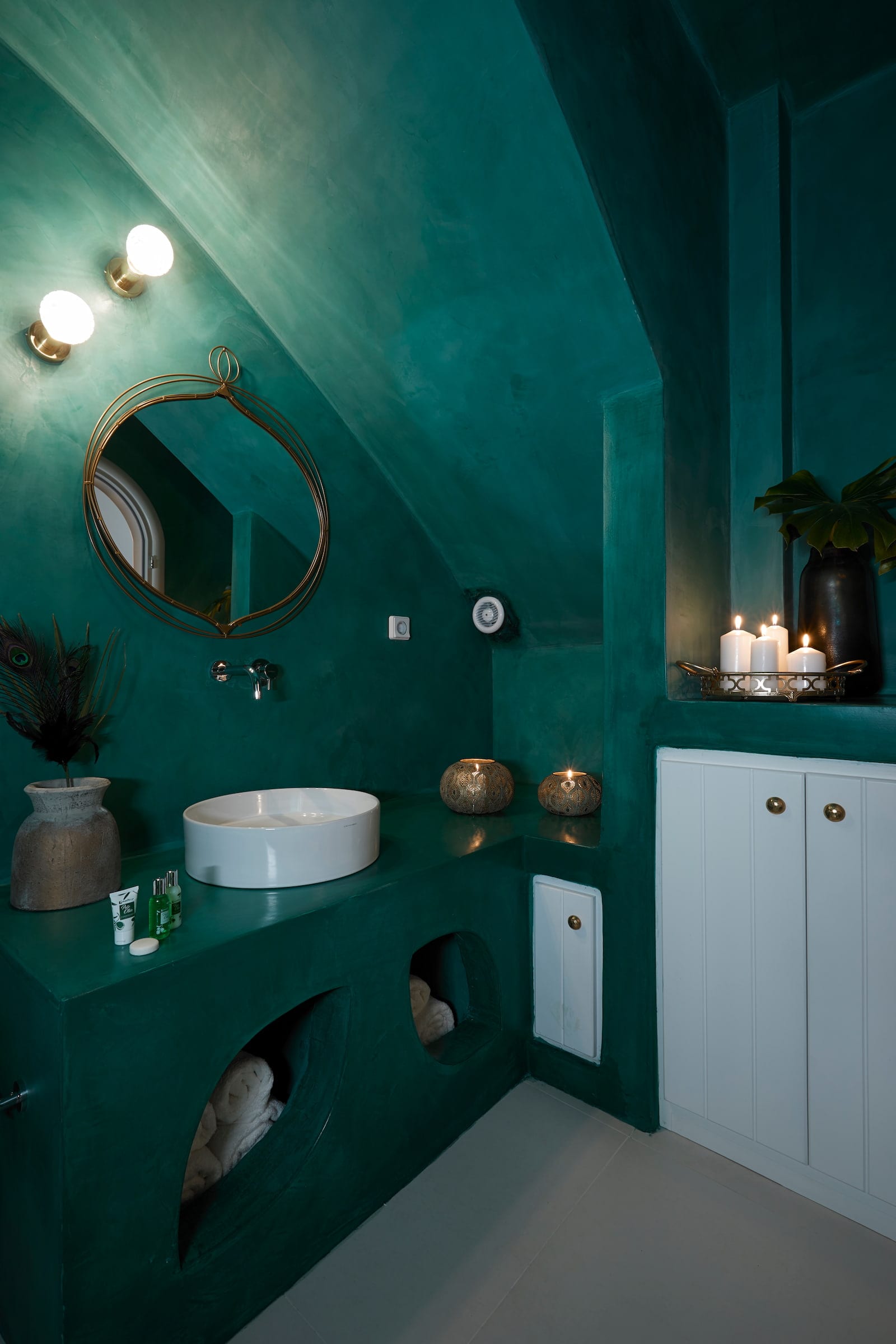 Emerald-green bathroom with a brass mirror, vessel basin, pillar candles and whitewashed cabinet