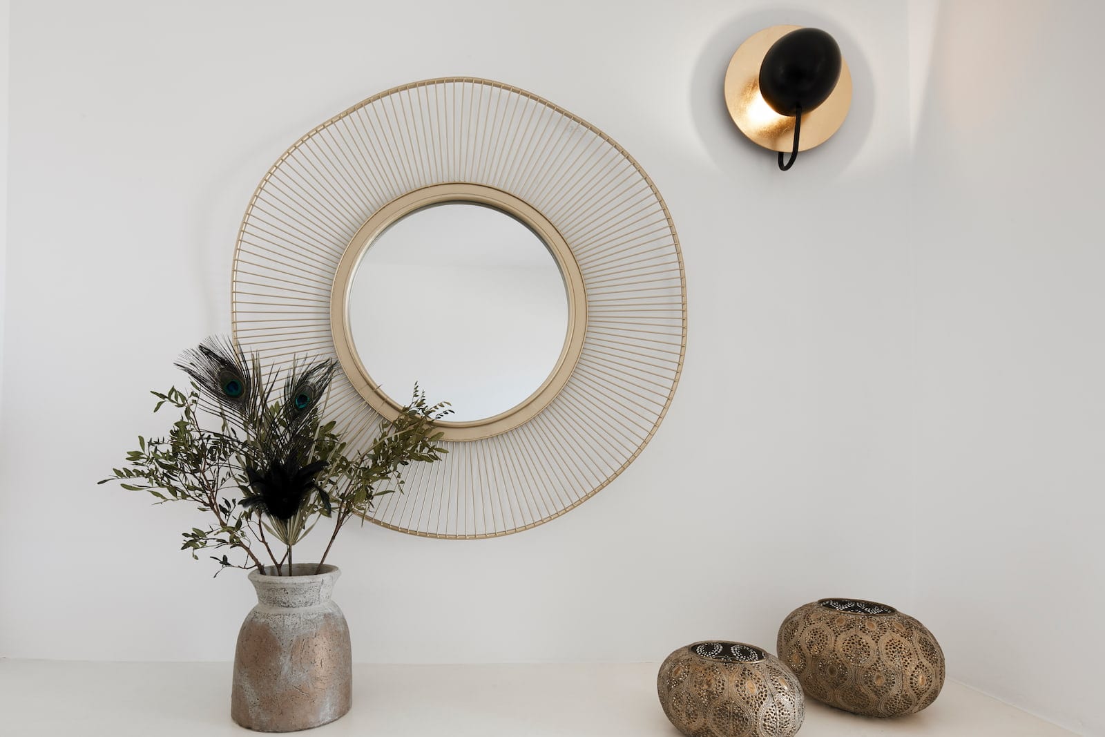 Round gold sunburst mirror, brass wall light and pierced tea-light holders on a white console