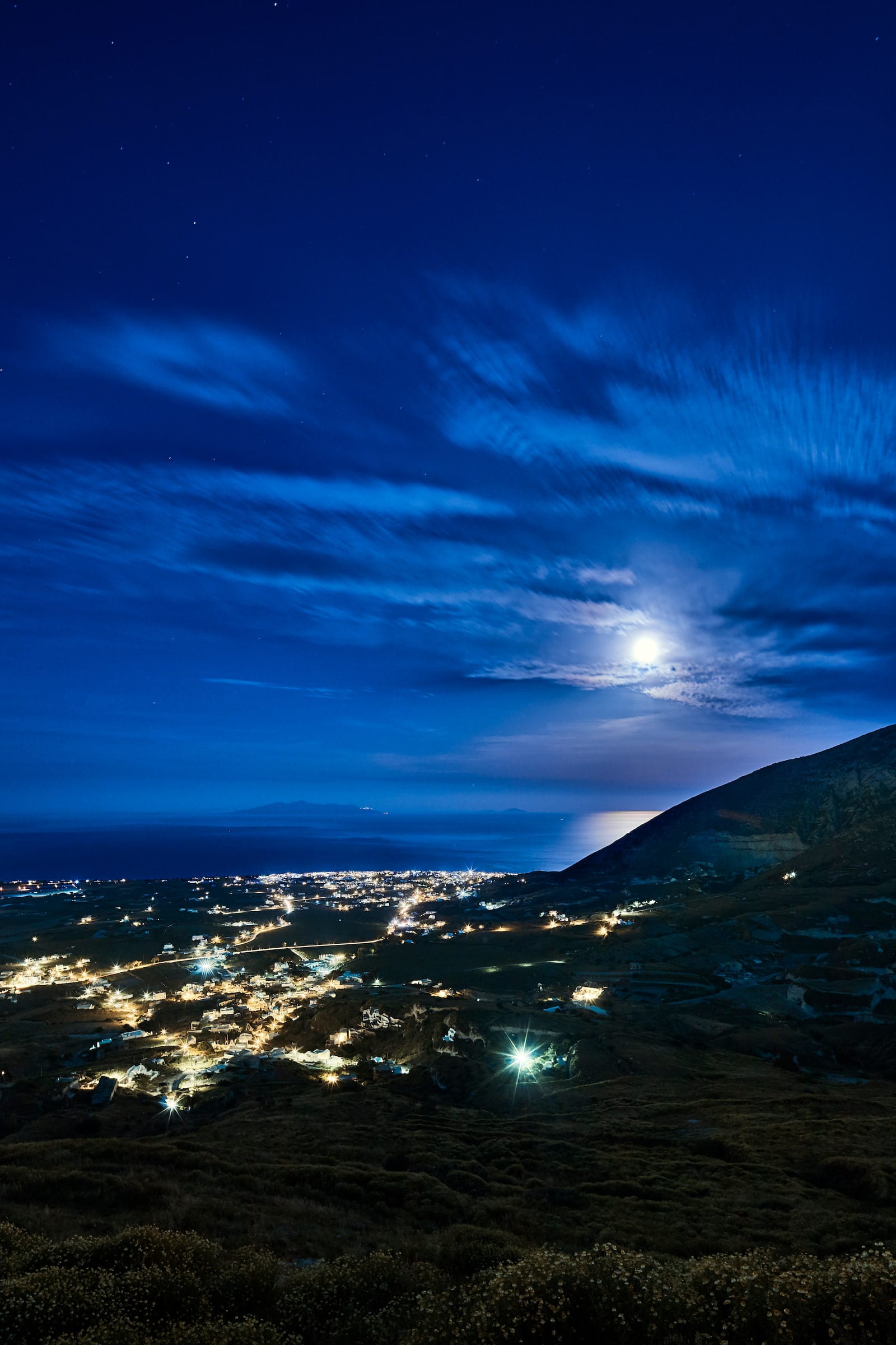 Nighttime view over Pyrgos village lights and the moonlit Aegean from Santorini's hillside