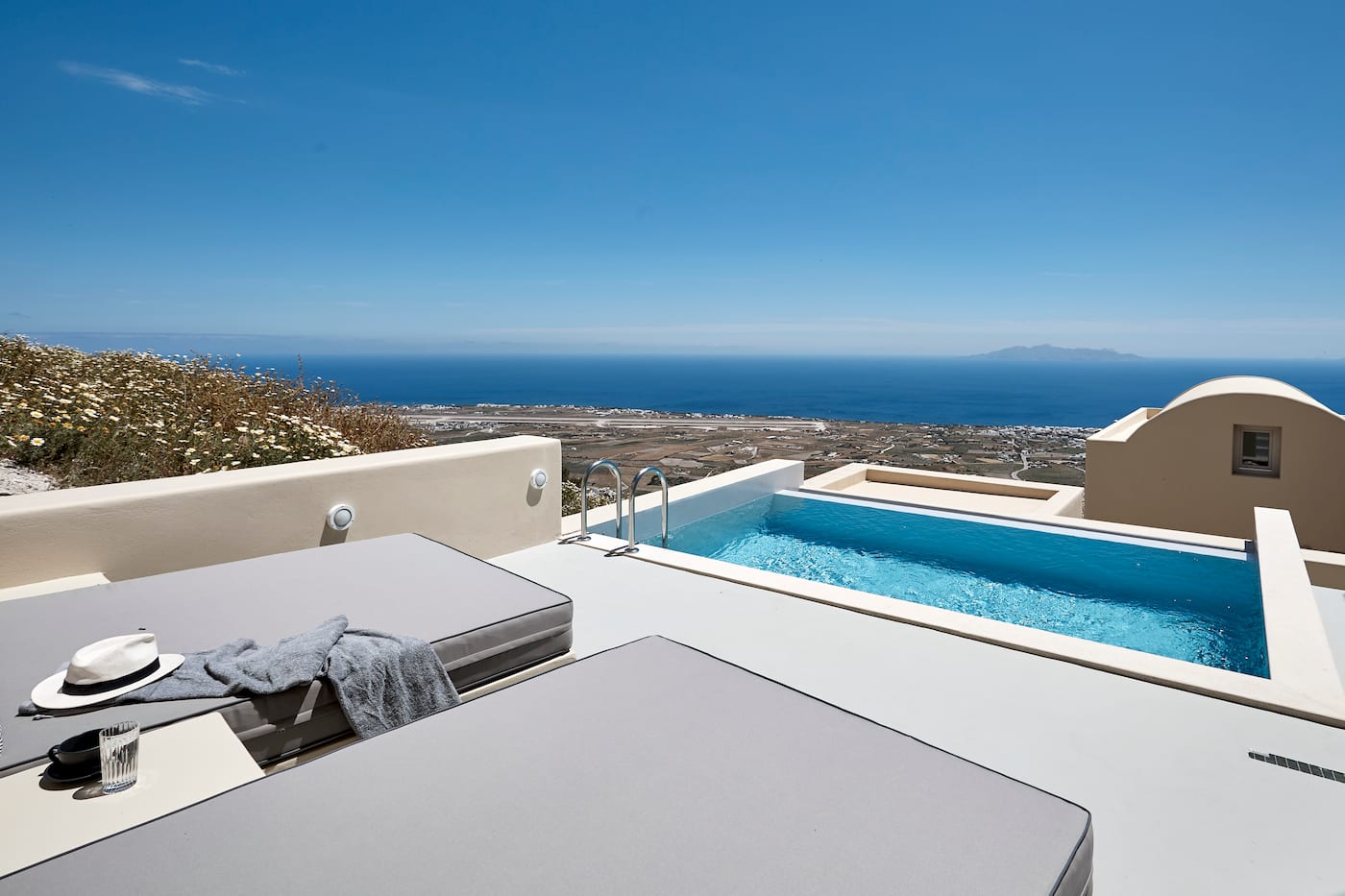 Grey sun loungers and a private pool on a terrace facing the deep blue Aegean