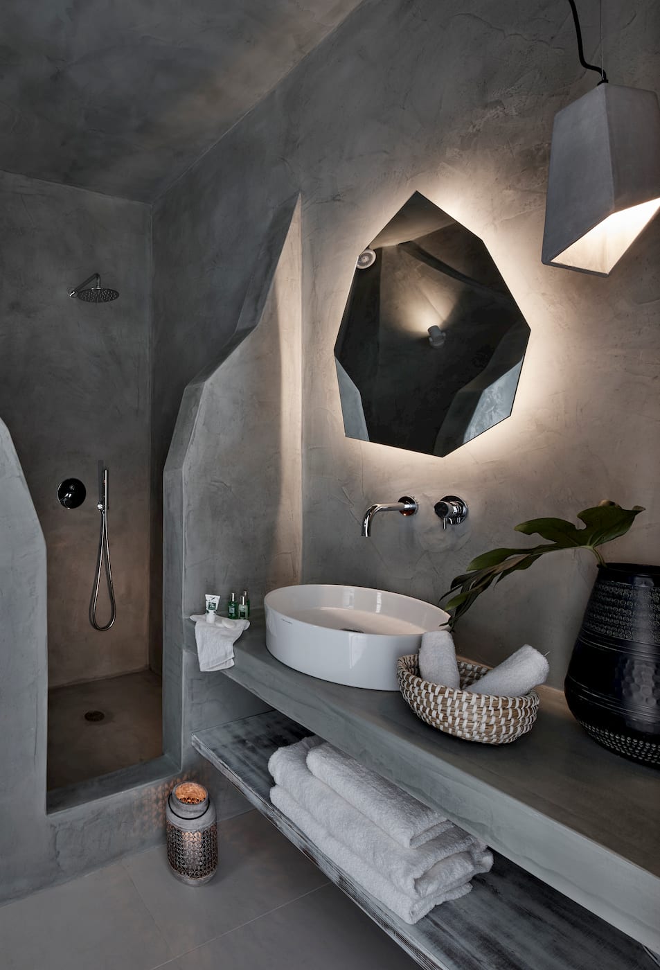 Grey microcement bathroom with a walk-in rain shower, vessel sink and backlit faceted mirror