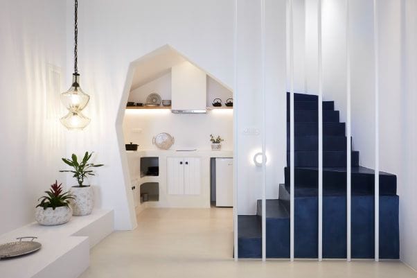 Whitewashed kitchenette tucked into an arched niche beside a cobalt-blue staircase