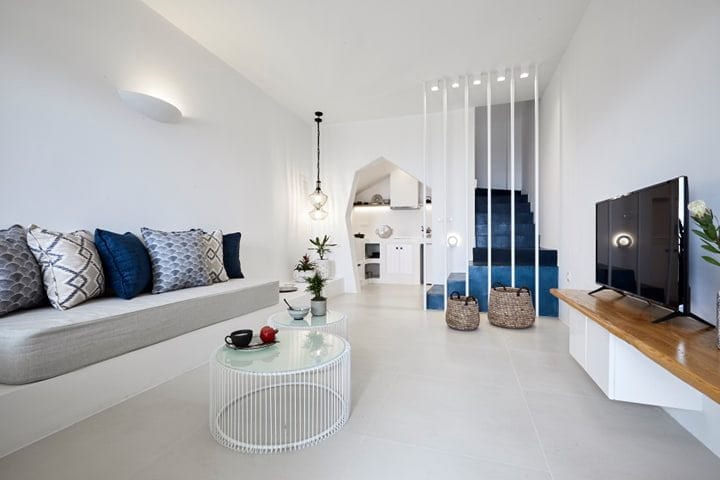 Bright living room with a built-in sofa, round glass tables, TV and cobalt-blue staircase