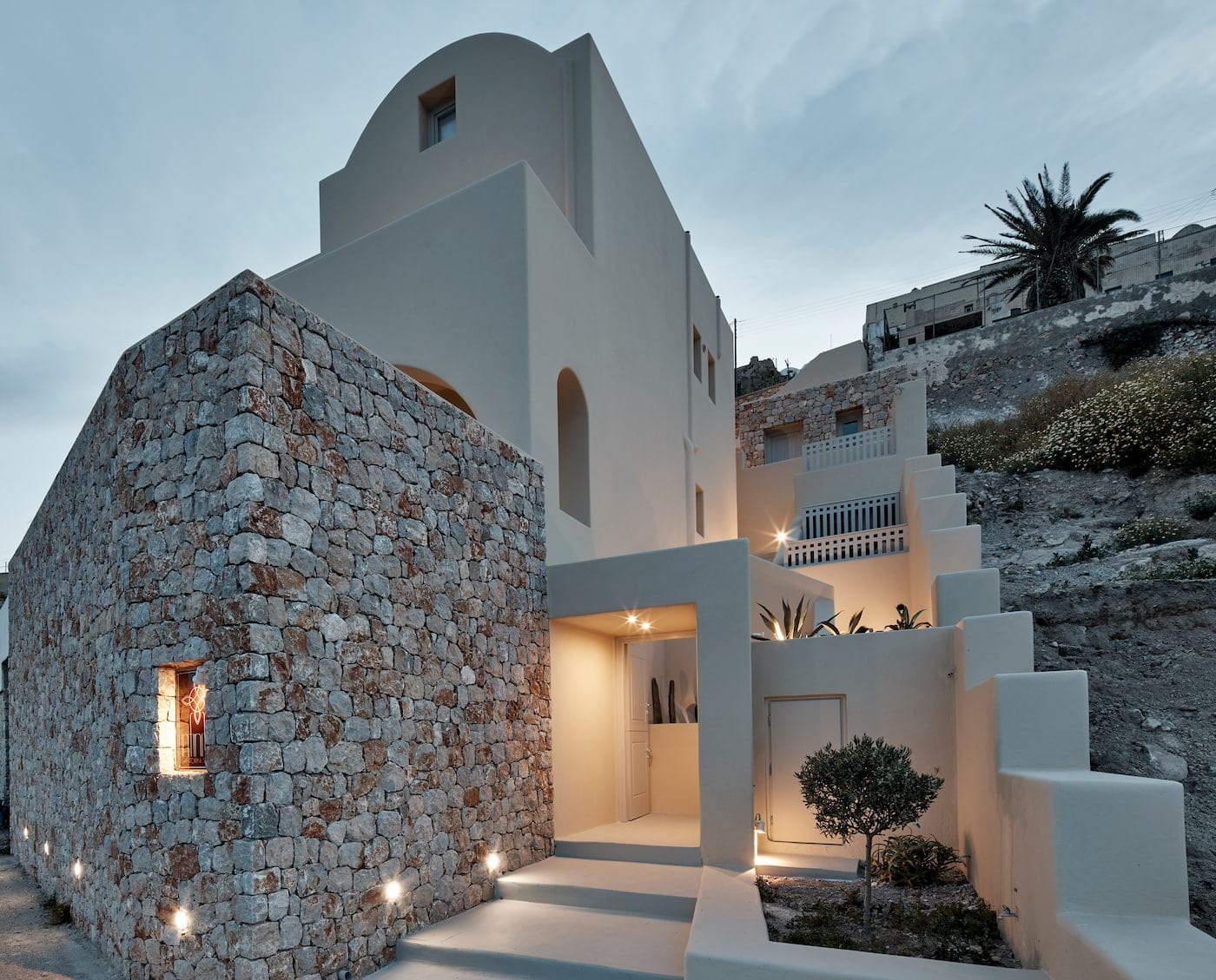 Dusk exterior of Suite Two showing natural-stone and whitewashed Cycladic architecture with a lit entrance