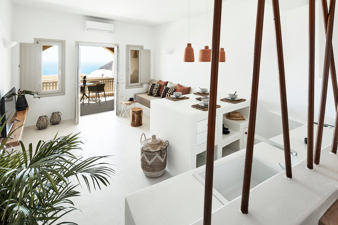 Open-plan living area with terracotta pendants and a terrace doorway framing the Aegean Sea