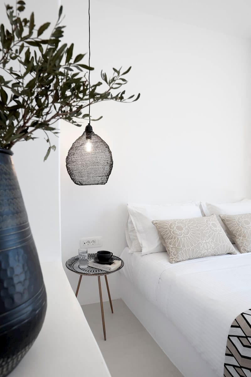 Whitewashed bedroom corner with an olive branch, black wire pendant lamp and a slim tripod bedside table