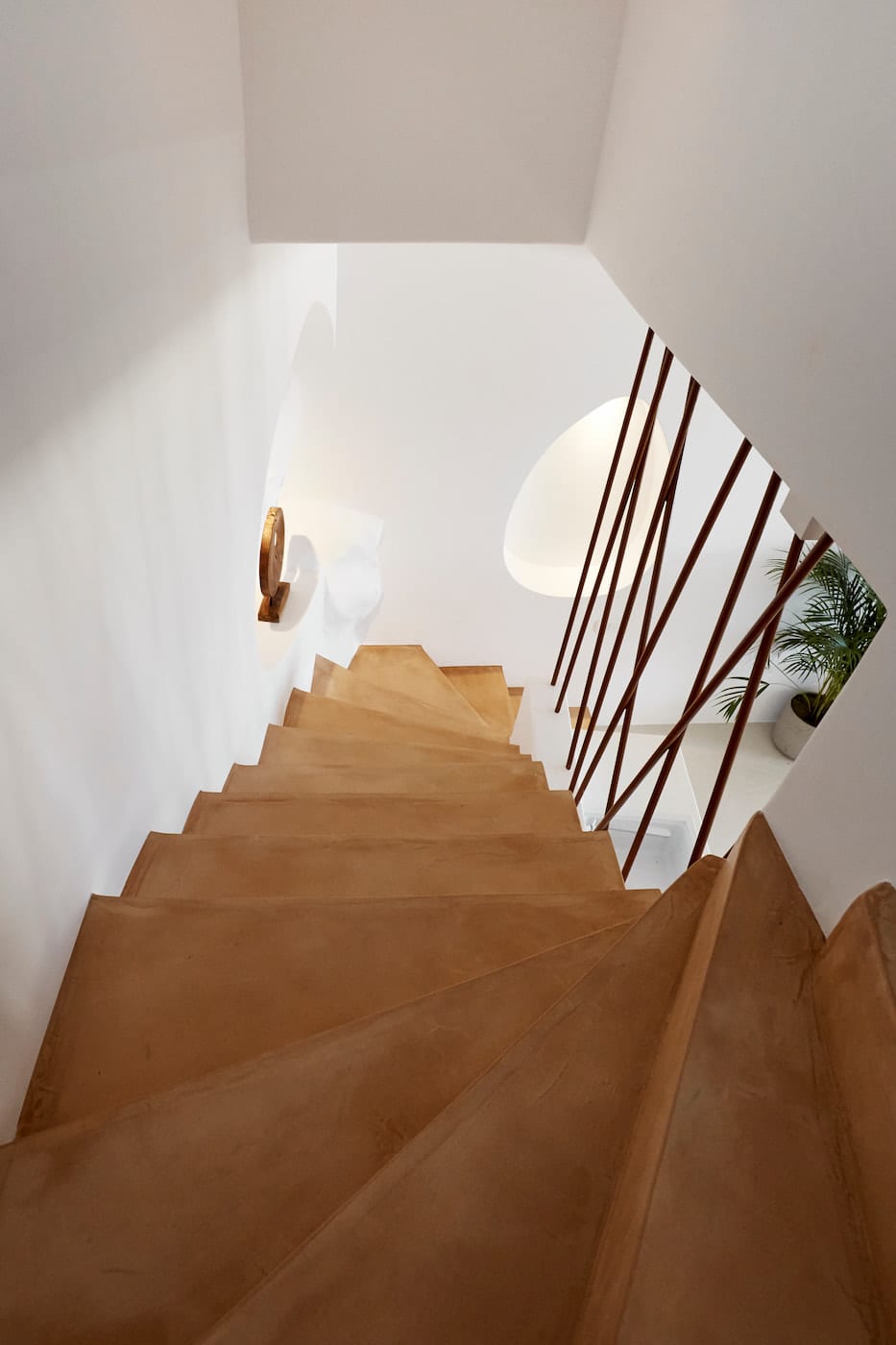 Ochre polished-concrete staircase descending past a wooden sconce and sculpted egg-shaped wall niche