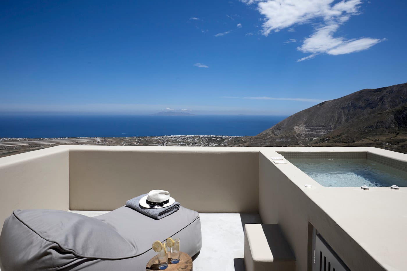 Private terrace jacuzzi and bean-bag lounger overlooking the Aegean, mountainside and Santorini village below