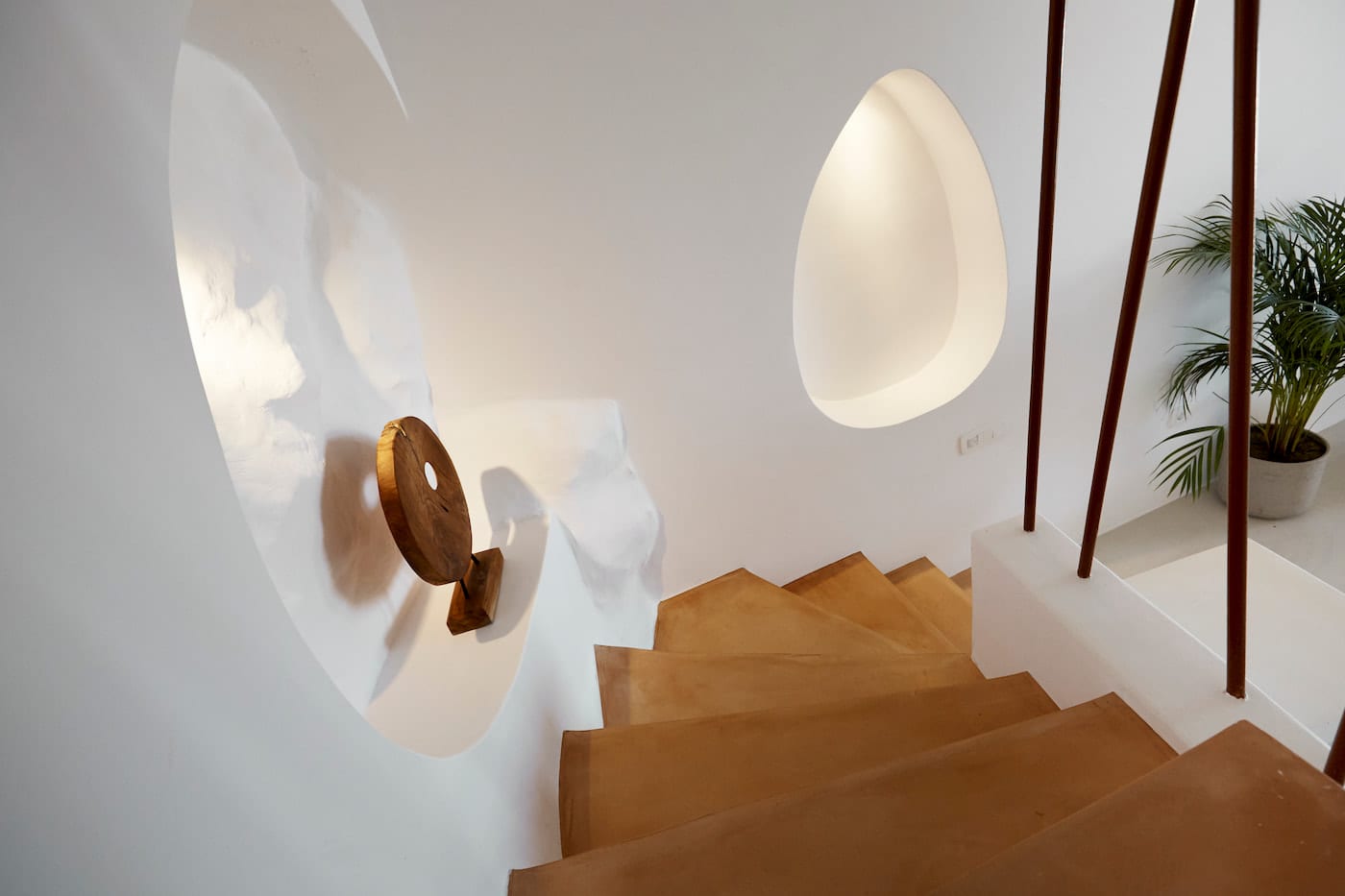 Sunlit stairwell detail with a round wooden handrail, glowing niche and slender timber balusters