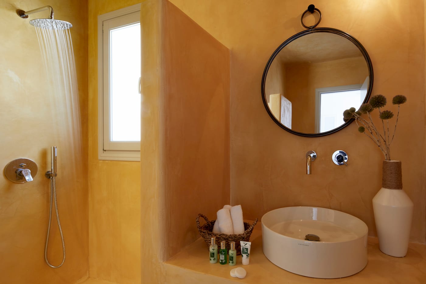 Ochre tadelakt bathroom with a rain shower, round black mirror and a white vessel basin