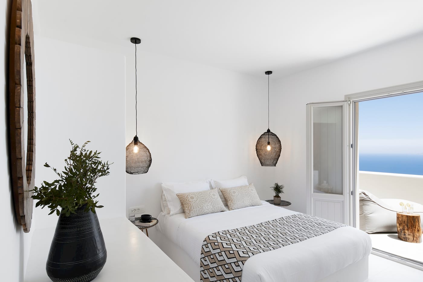 Bright bedroom with a geometric bed runner opening onto a terrace and boundless Aegean sea view