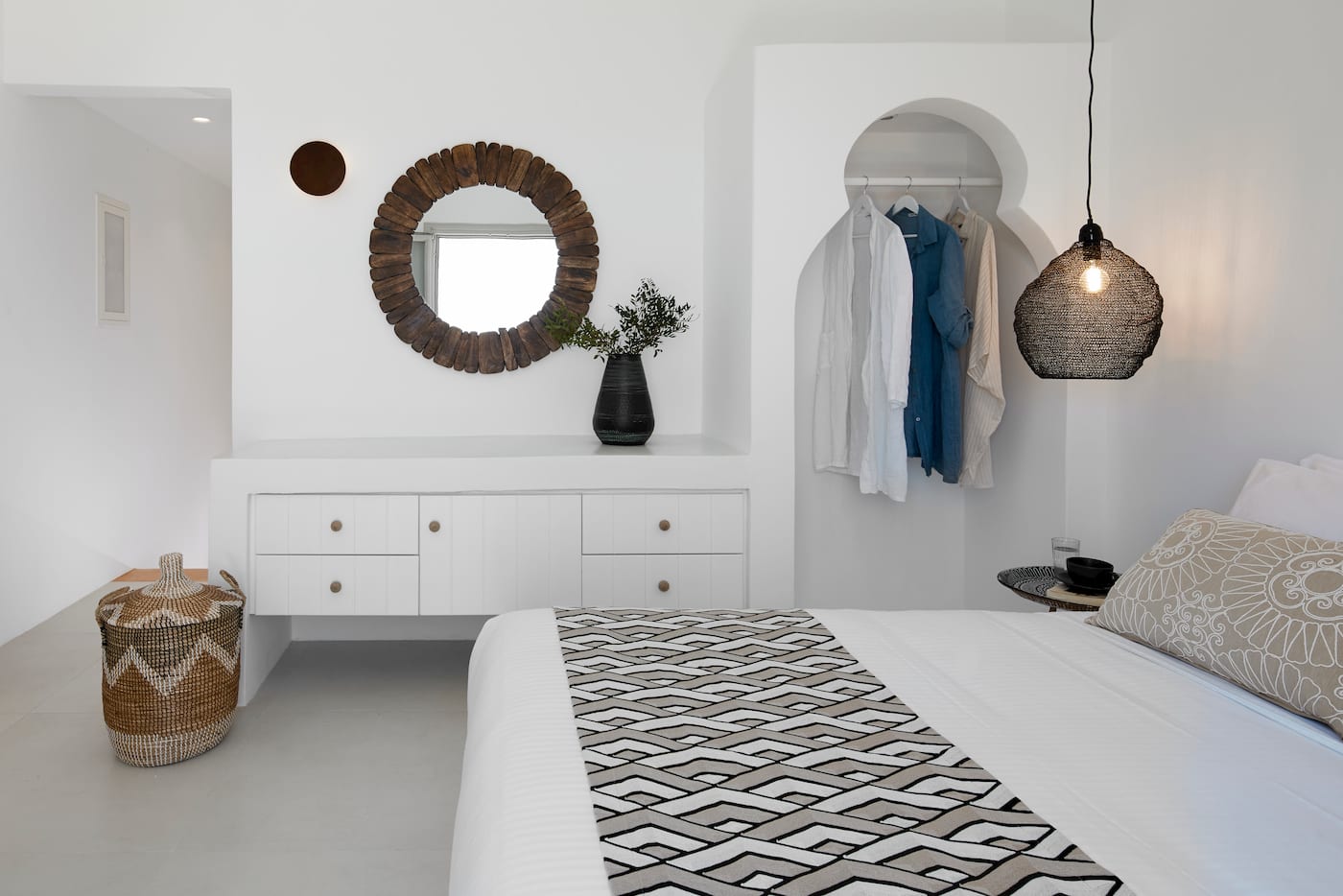 Bedroom with a driftwood mirror, built-in dresser and an arched niche wardrobe holding linen garments