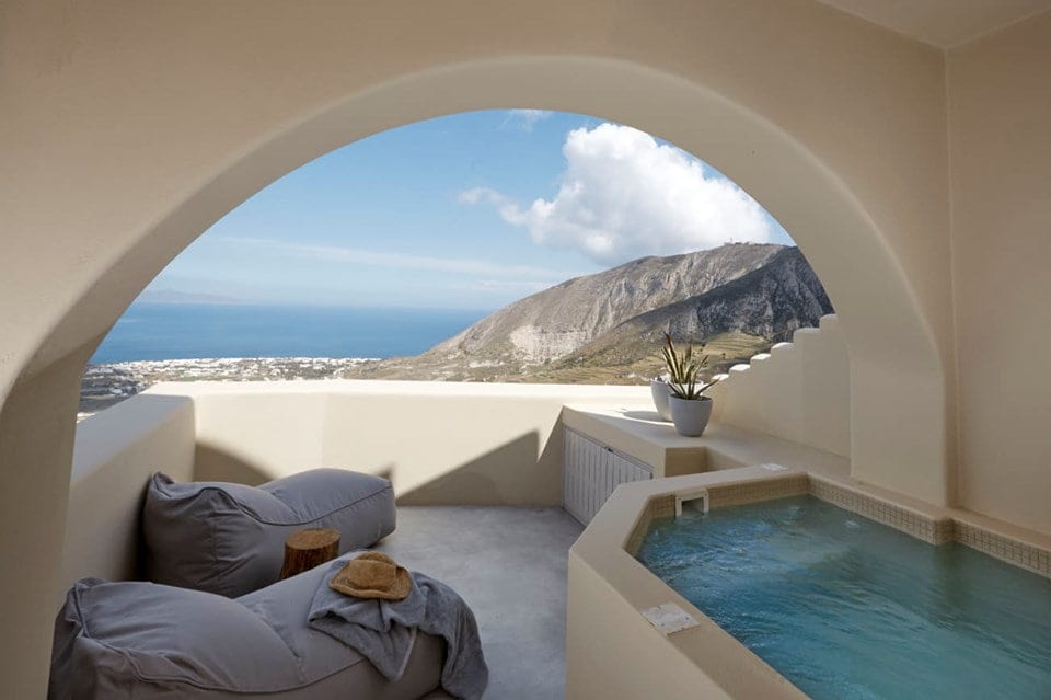 Suite Two arched terrace with bean bags and a heated jacuzzi framing Santorini's mountain and sea view