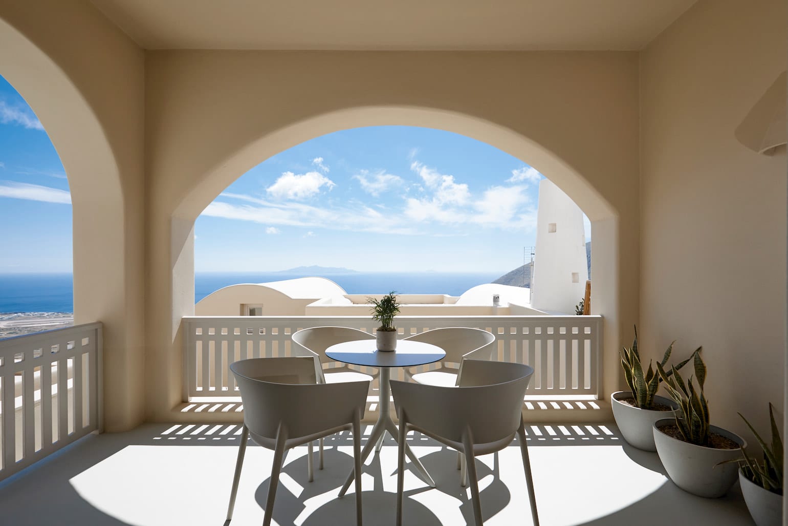 Suite Three's arched Pyrgos terrace with a bistro table framing sweeping Aegean sea and distant island views